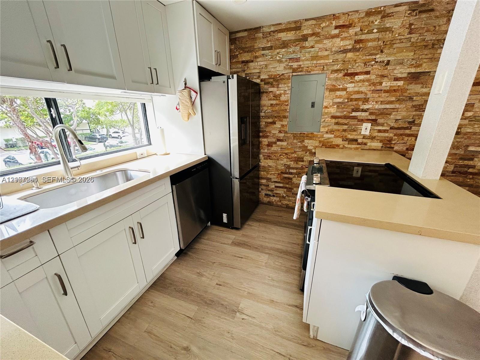 Kitchen featuring white shaker cabinetry, stacked stone backsplash, stainless steel appliances, wood-finish flooring, and solid-surface countertops