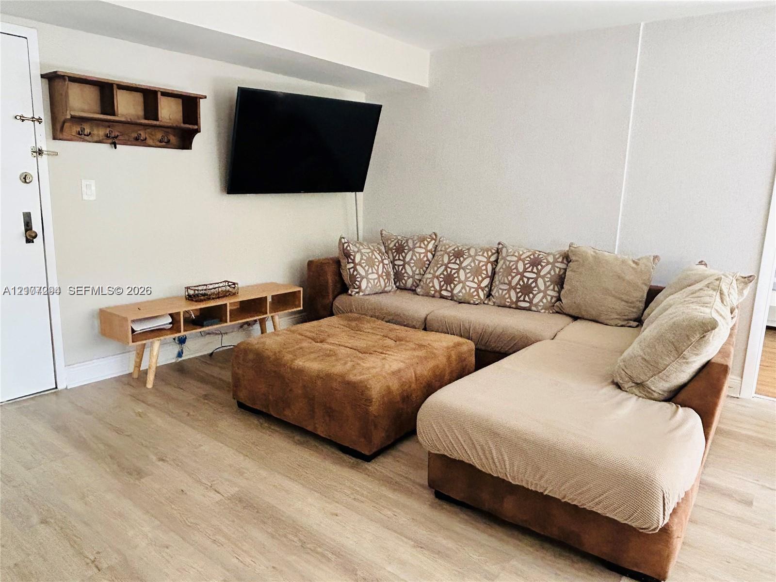 Interior space featuring neutral wall tones, wood-finish flooring, and a wall-mounted wooden storage shelf with integrated hooks