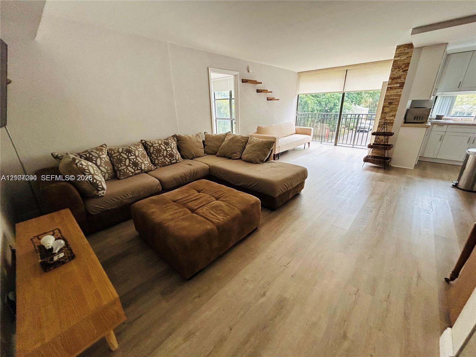 Open-concept interior featuring wood-finish flooring, a floor-to-ceiling stone accent column, sliding glass doors to a balcony, and white cabinetry with a quartz countertop