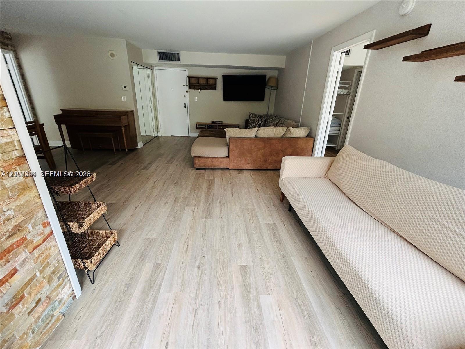 Open-concept interior featuring wood-finish flooring, a textured stone accent wall, and dual wall-mounted floating shelves