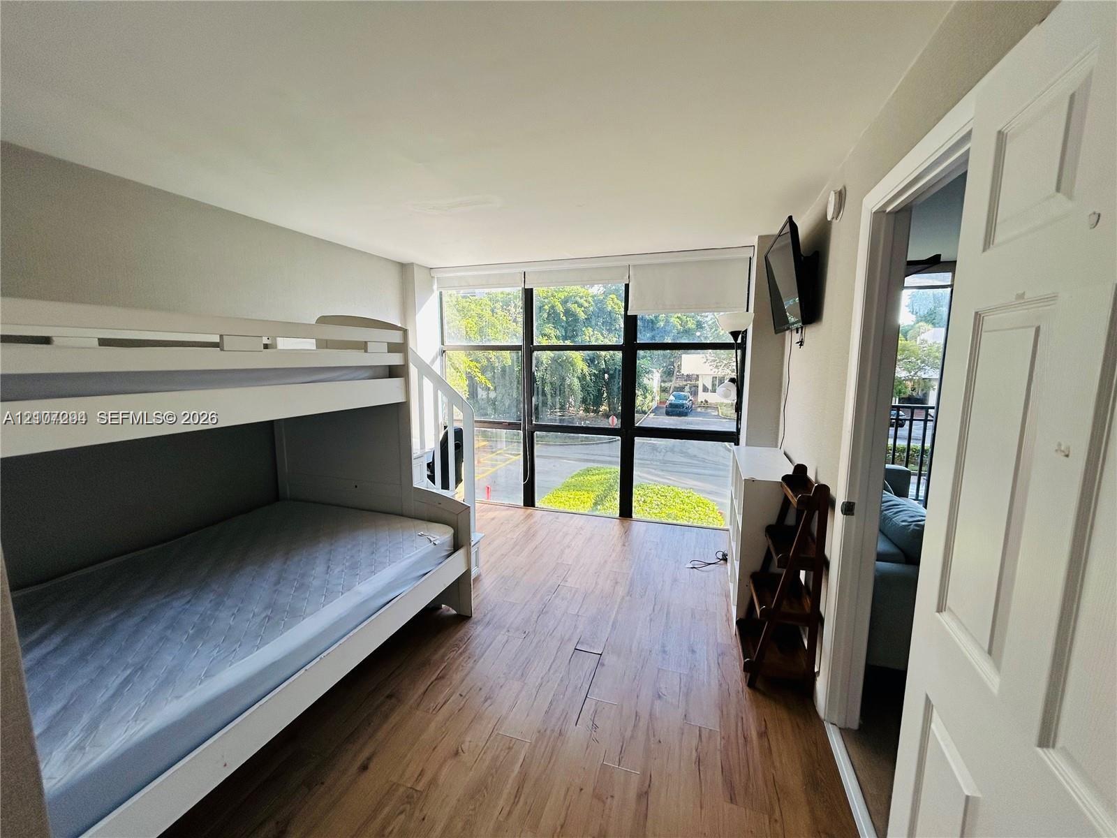 Floor-to-ceiling windows with black metal framing, wood-finish flooring, and white paneled interior door