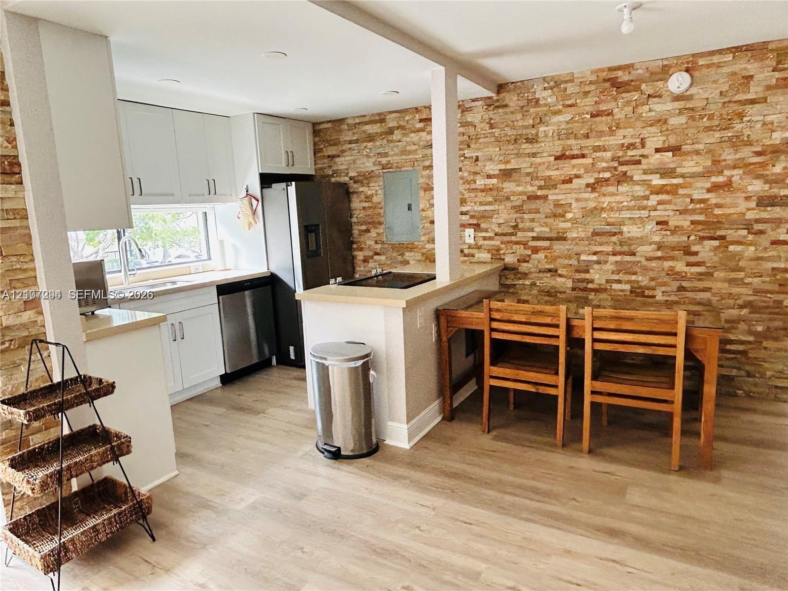 Kitchen featuring stacked stone accent wall, white cabinetry, integrated stainless steel appliances, and wood-finish flooring