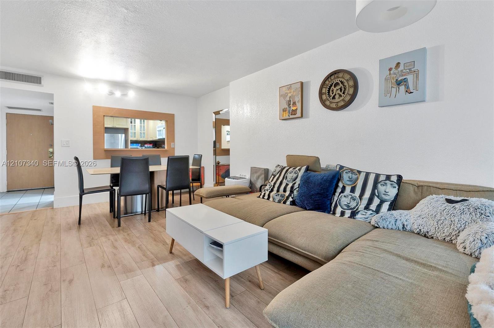 Open-concept interior featuring light-tone wood-finish flooring, a pass-through window with wood trim, neutral wall finishes, and a contemporary ceiling-mounted light fixture