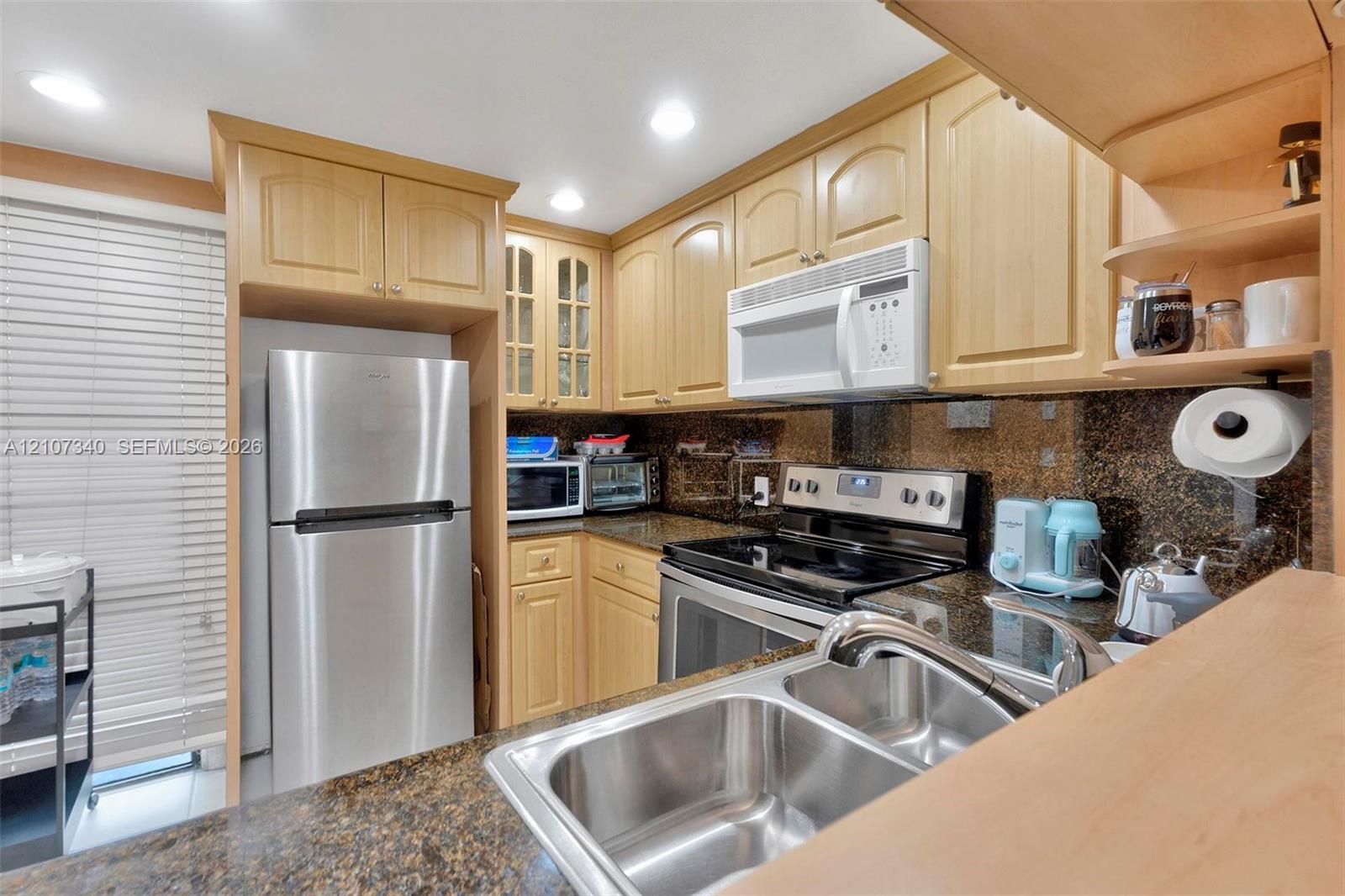 Kitchen featuring light-finish cabinetry, stone-surface countertops, stainless steel appliances, a double-basin sink, and glass-paneled upper cabinets