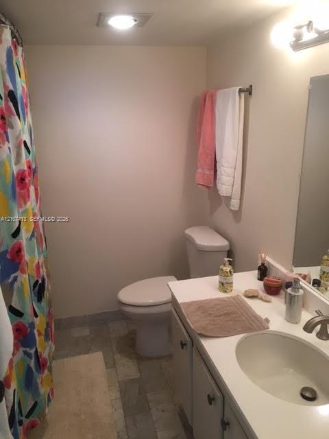 Bathroom featuring a single-basin vanity with a solid-surface countertop, an undermount sink, multi-tone tile flooring, and a wall-mounted light fixture