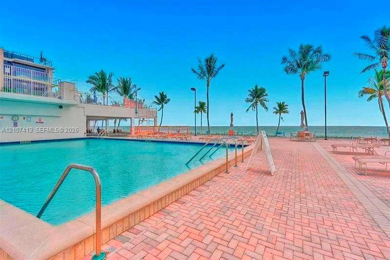 Oceanfront swimming pool featuring a brick-paver deck, metal ladder entry, and mature palm trees