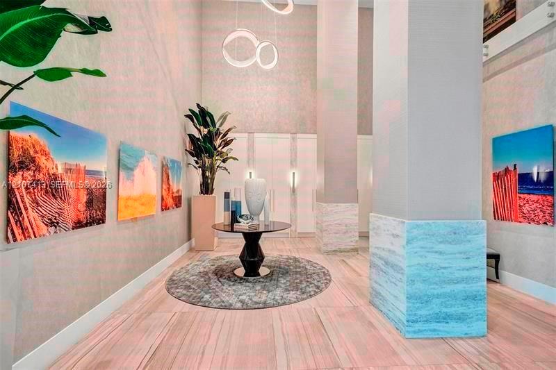 High-ceiling foyer featuring stone tile flooring, a prominent structural column with stone detailing, minimalist ring pendant lighting, and floor-to-ceiling built-in cabinetry