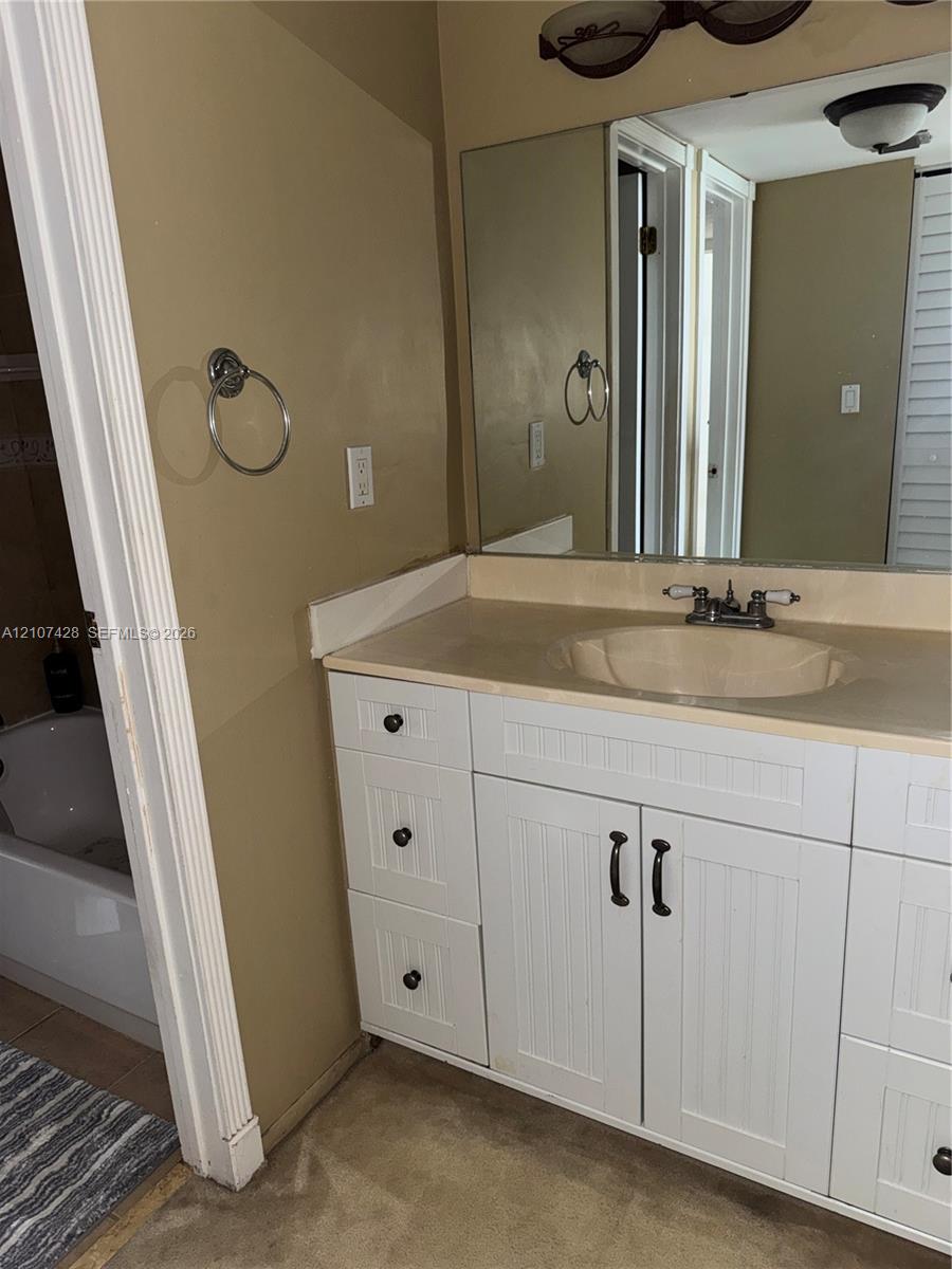 White vanity with beadboard-style cabinetry, solid-surface countertop, integrated basin, chrome dual-handle faucet, and oversized wall-mounted mirror