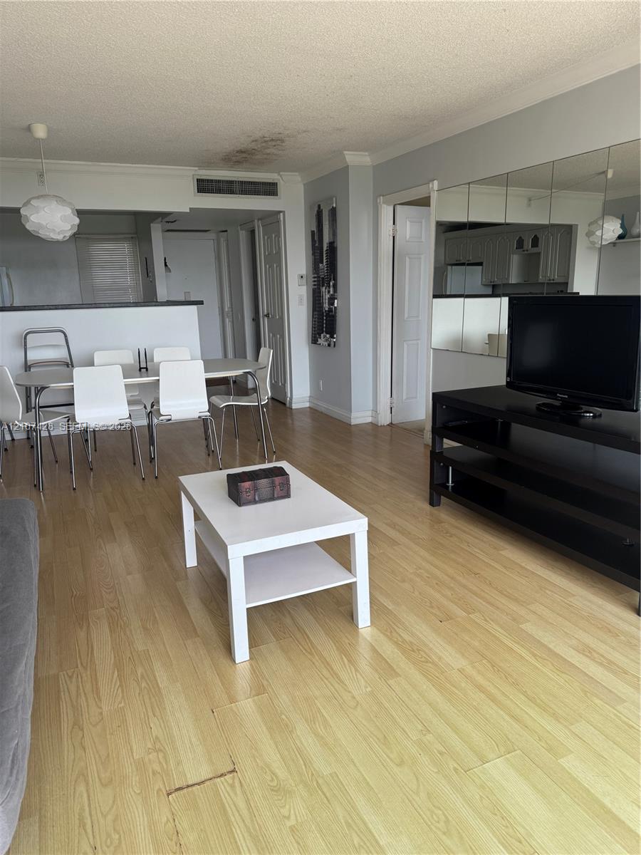 Open-concept interior featuring light wood-finish flooring, a mirrored wall accent, and a built-in kitchen pass-through counter