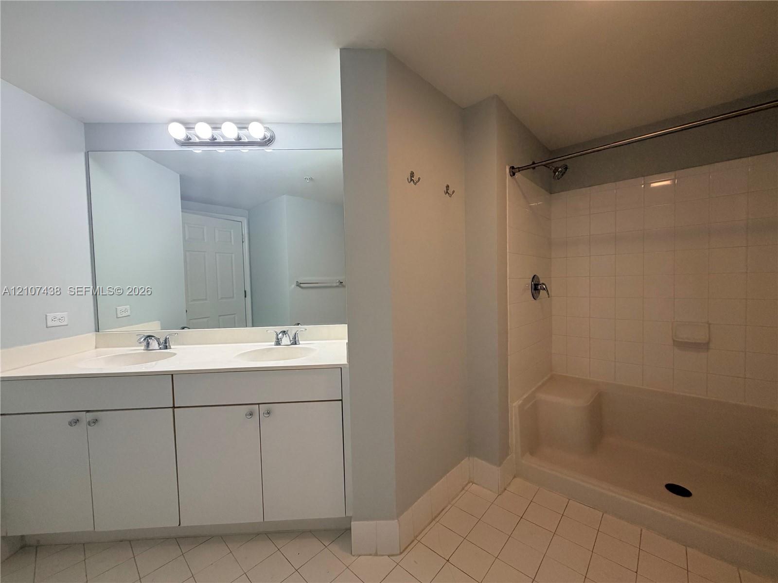 Double vanity with white cabinetry, oversized wall mirror, tiled shower and tub combination, and ceramic tile flooring