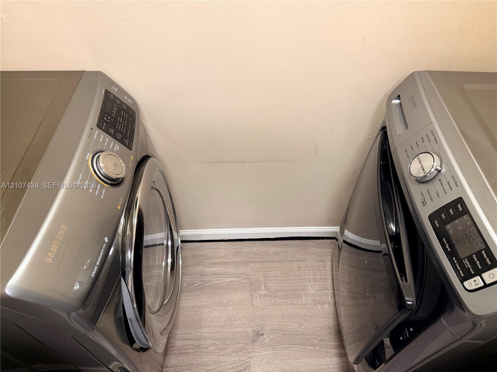 Laundry space featuring metallic-finish side-by-side Samsung appliances and wood-finish flooring