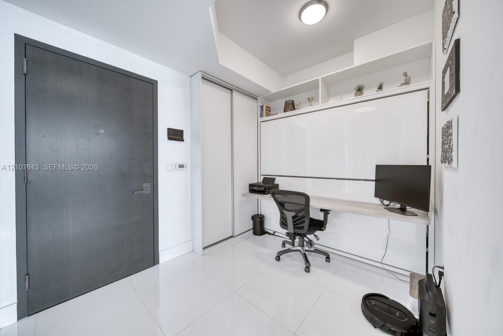 Integrated built-in cabinetry with desk surface, glossy tile flooring, smooth-finish ceiling with recessed lighting, and a dark-finish solid-core entry door