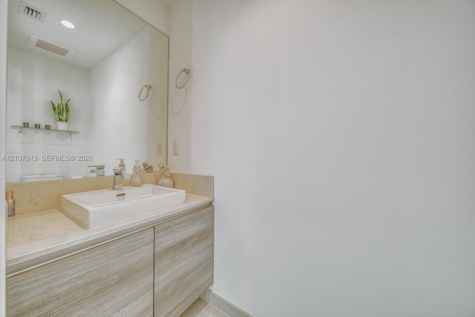 Floating vanity with a light wood-finish cabinet, rectangular vessel sink, solid-surface countertop, and an expansive wall-mounted mirror