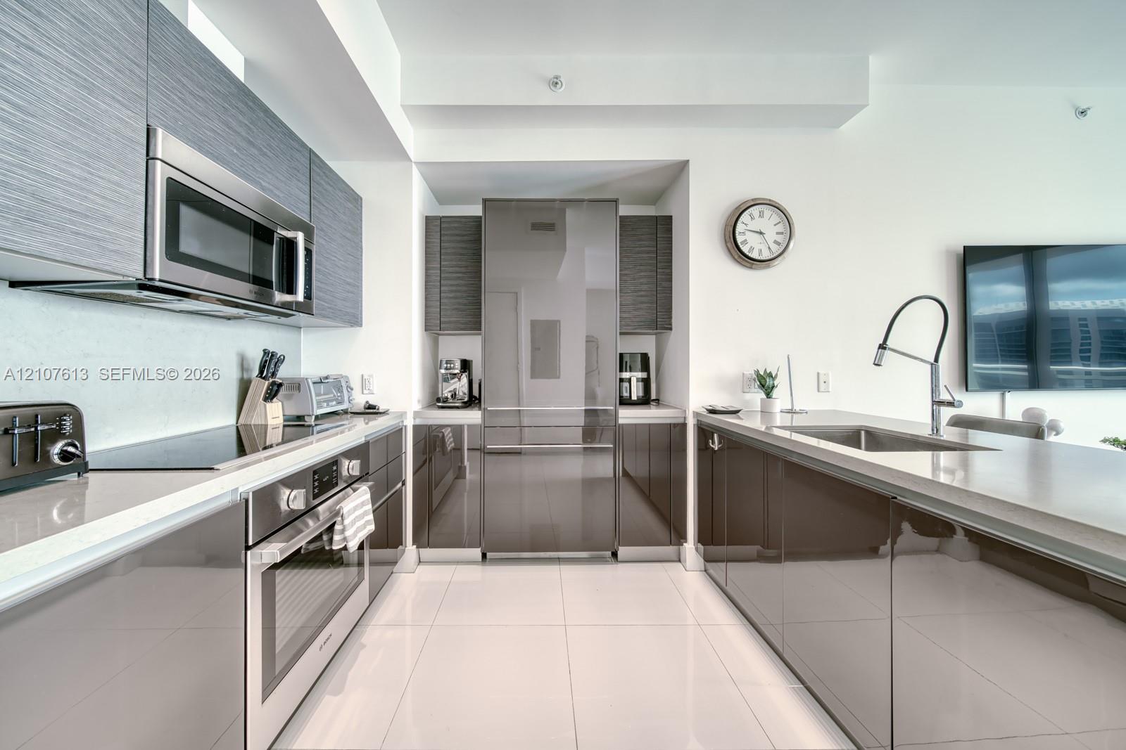 Modern kitchen featuring high-gloss cabinetry, stainless steel appliances, integrated refrigerator, stone-surfaced countertops, and a stainless steel gooseneck faucet