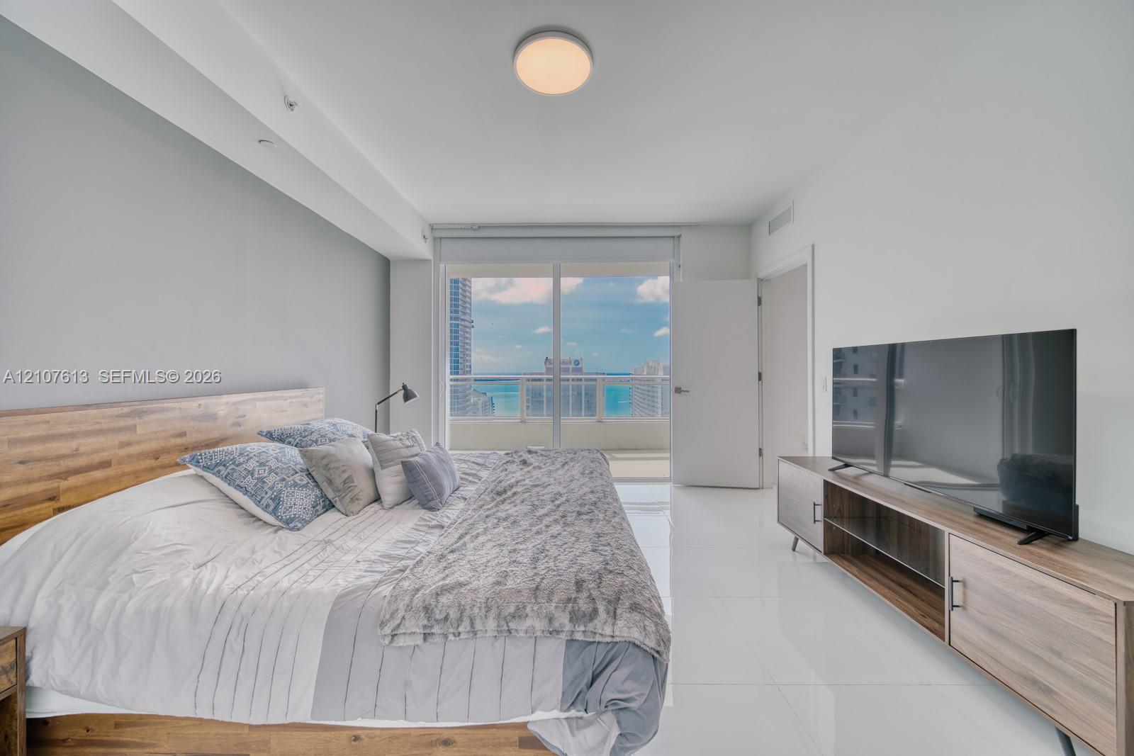 Floor-to-ceiling glass sliding doors opening to a balcony, high-gloss tile flooring, flush-mount ceiling lighting, and expansive wall space