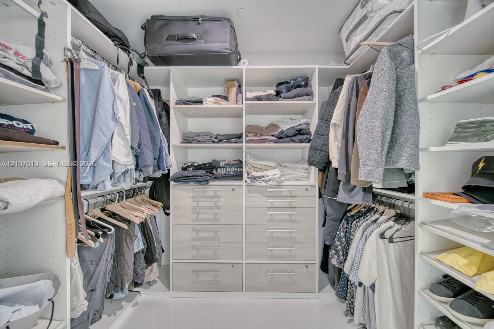 Custom walk-in closet featuring white floor-to-ceiling shelving, integrated wooden-finish cabinetry, built-in organizers, and hanging rods