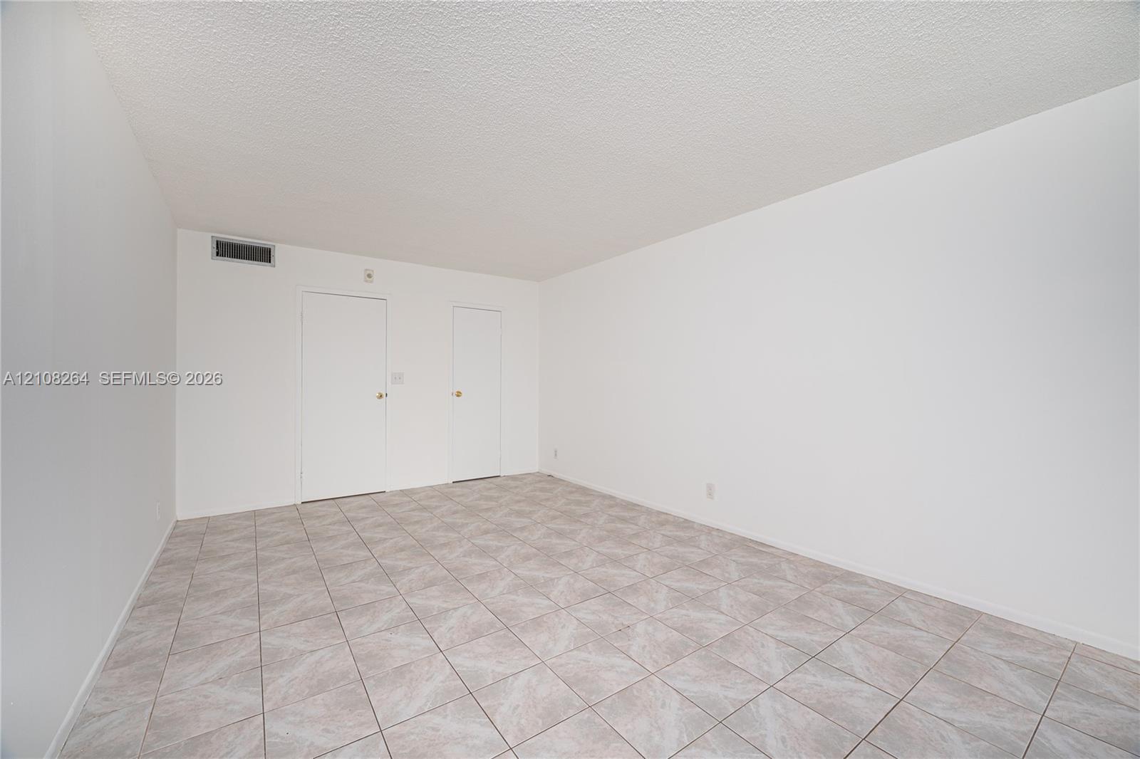 Neutral-toned tile flooring, textured ceiling, and dual interior doors finished in white