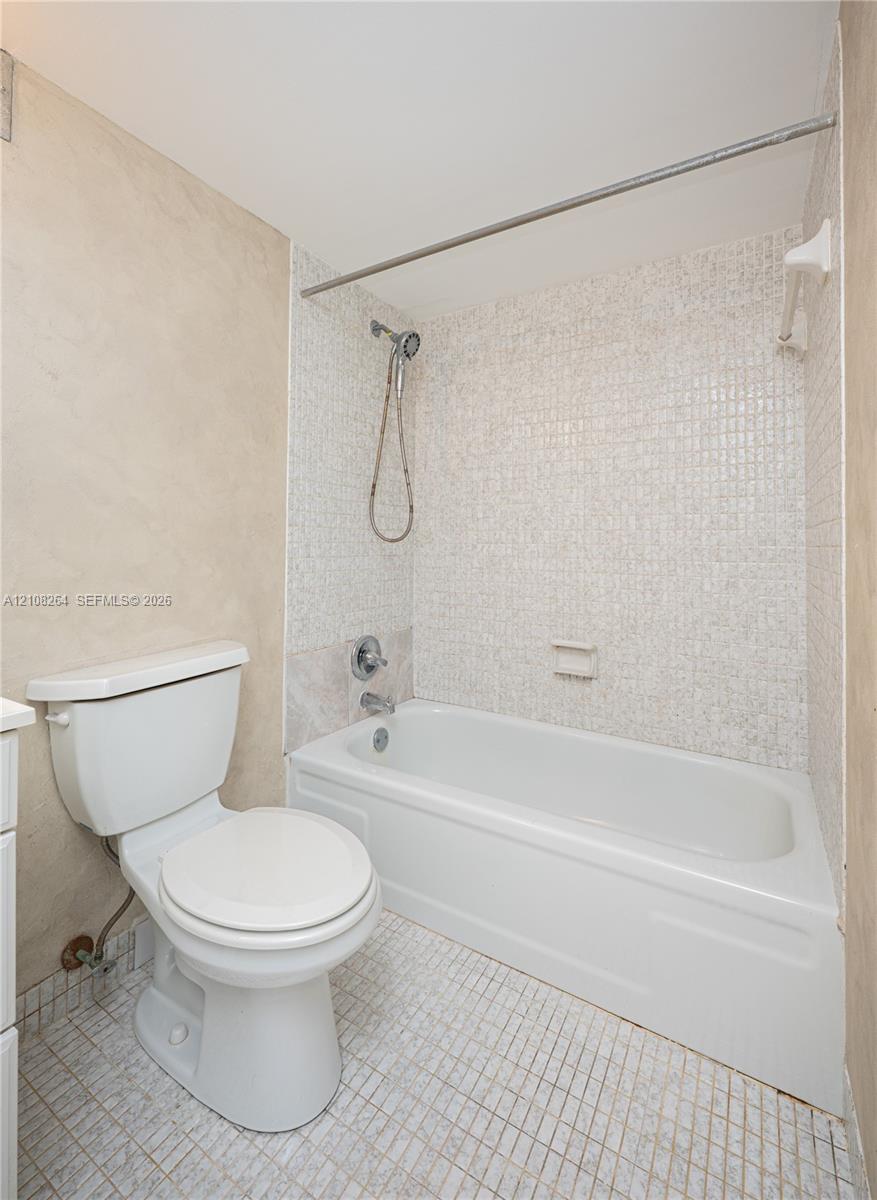 Bathroom featuring a white porcelain toilet, acrylic bathtub, wall-mounted handheld shower fixture, and mosaic tile surround