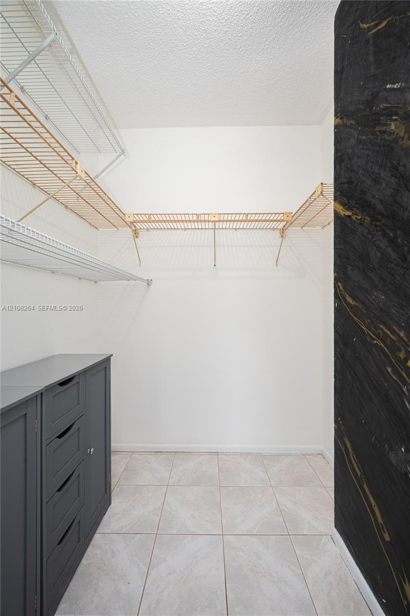 Storage area featuring white wire shelving, built-in dark gray cabinetry, and tile flooring, accented by a distinctive black and gold wall finish