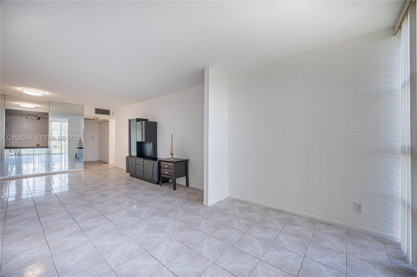 Neutral-toned tile flooring, floor-to-ceiling mirrored wall paneling, and a floor-to-ceiling window featuring vertical blinds