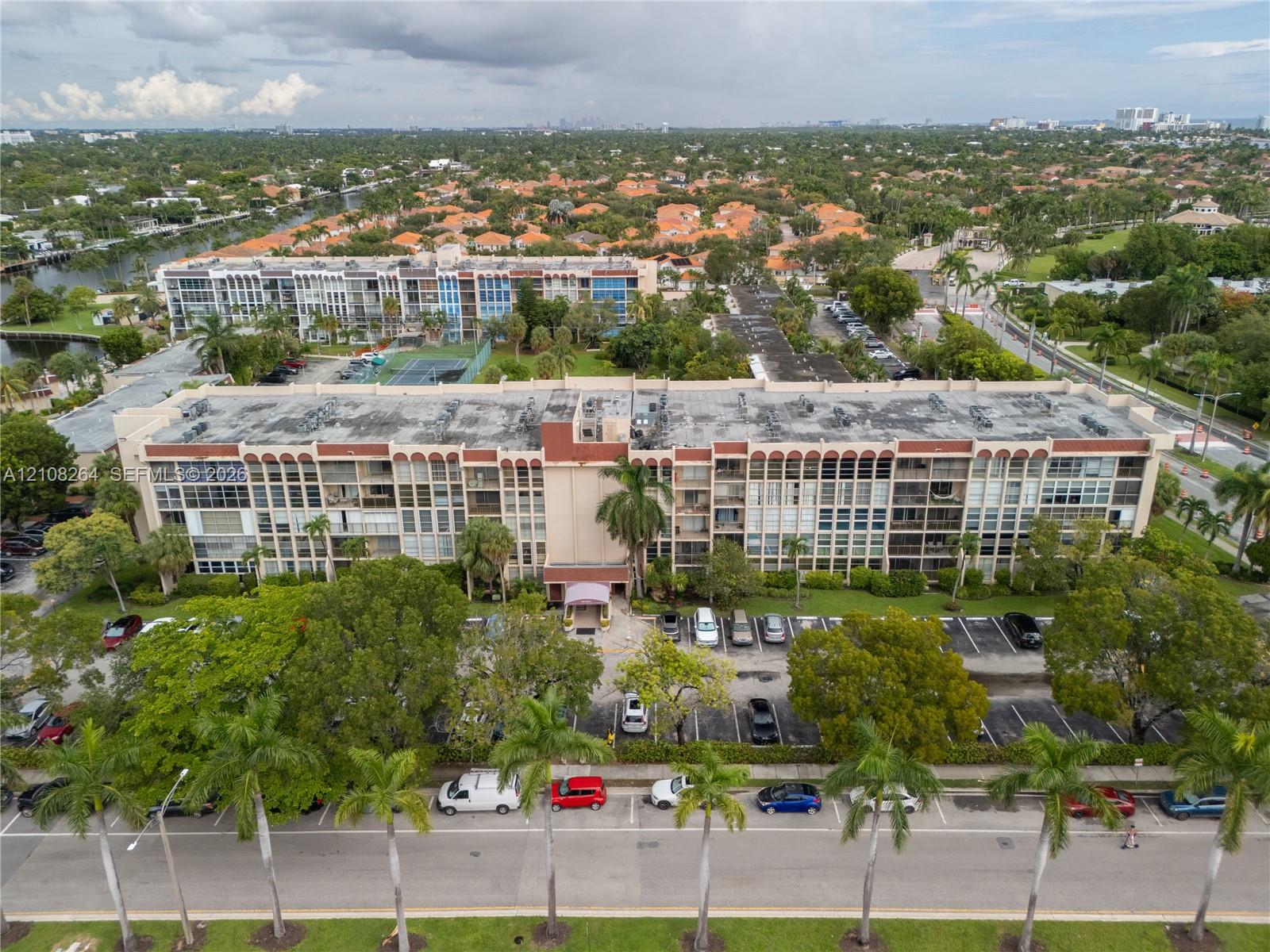 Multi-story residential building featuring a reinforced concrete facade with repetitive arched roofline details, ground-level covered entryway, and established mature landscaping
