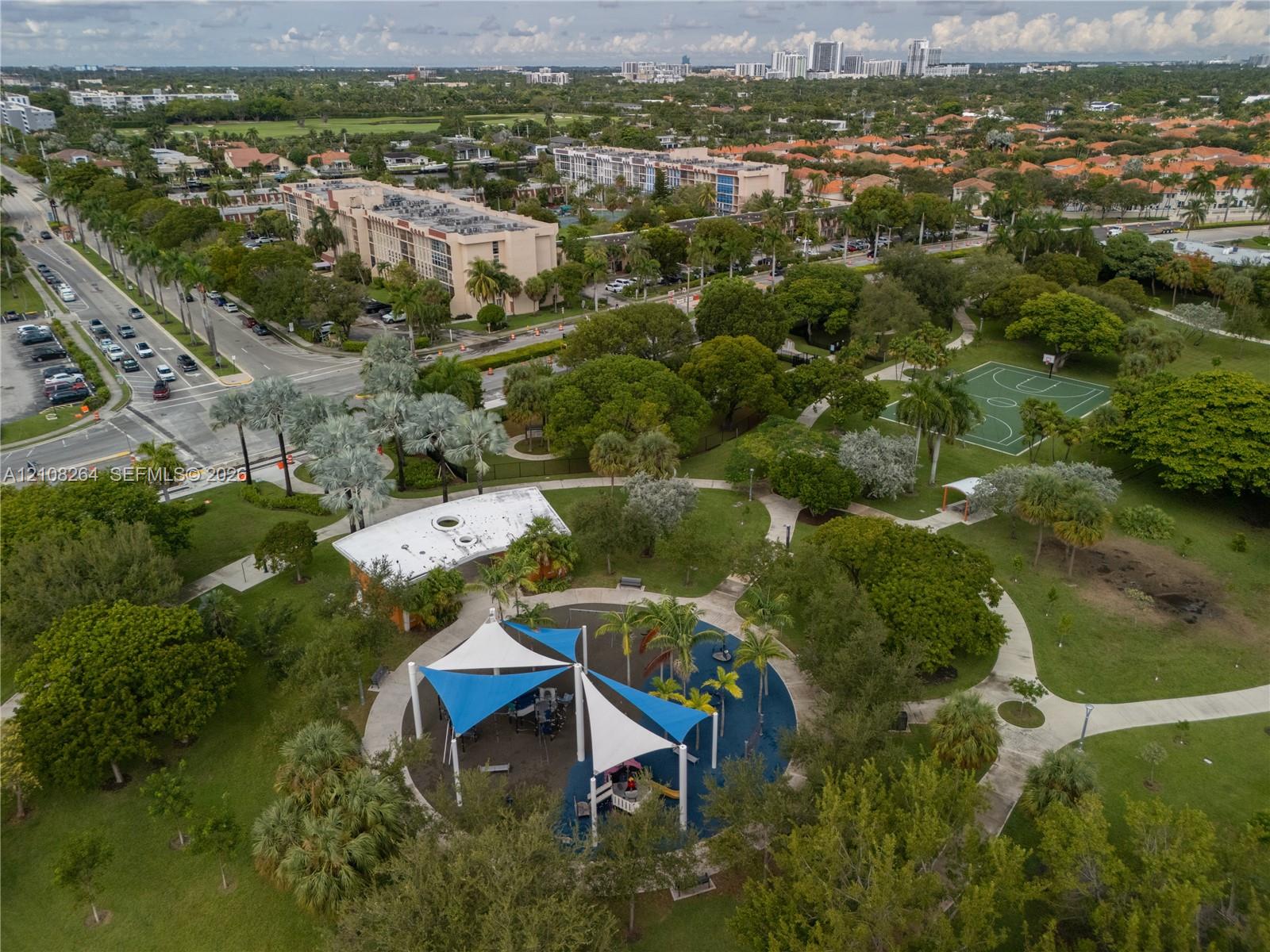 Extensive parkland featuring a playground with shade structures, a paved basketball court, concrete walking paths, and mature landscaping