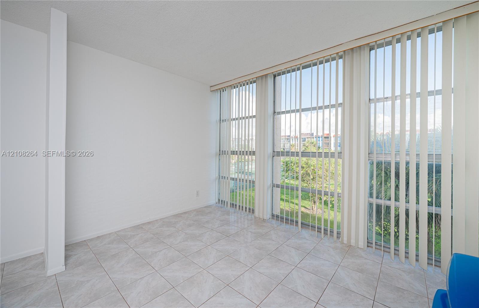 Interior space featuring neutral tile flooring, expansive floor-to-ceiling windows, and vertical blinds