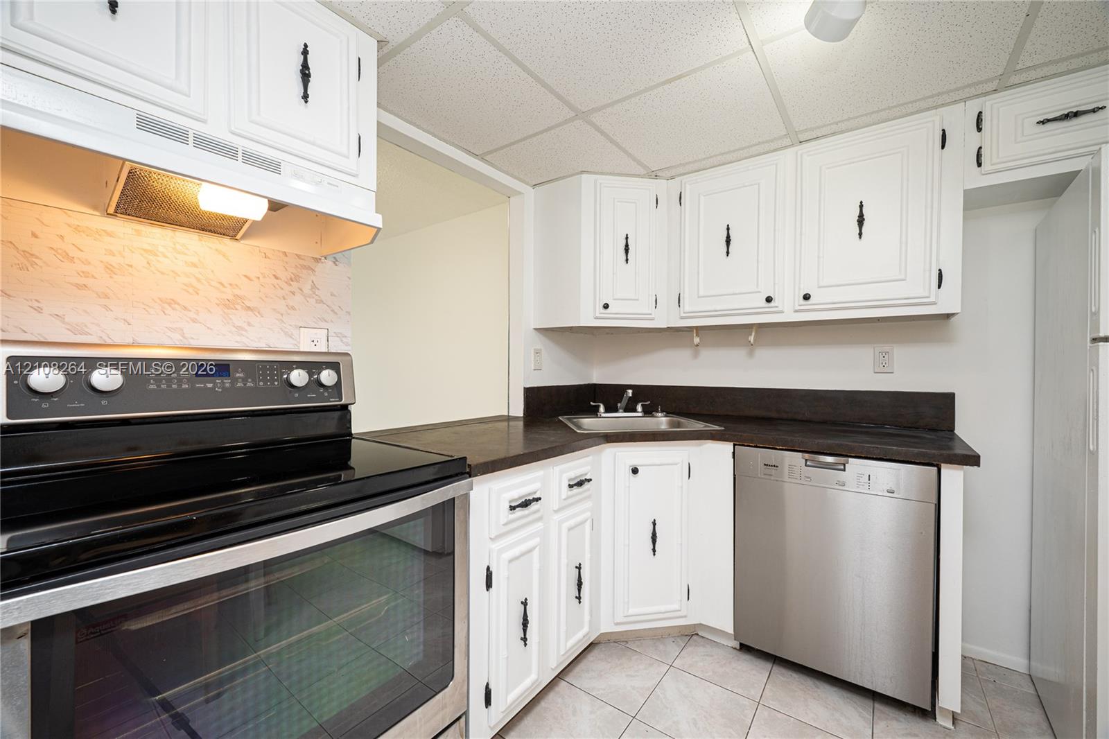 Kitchen featuring white cabinetry with black hardware, dark countertops, a stainless steel dishwasher, a black range, and tile flooring