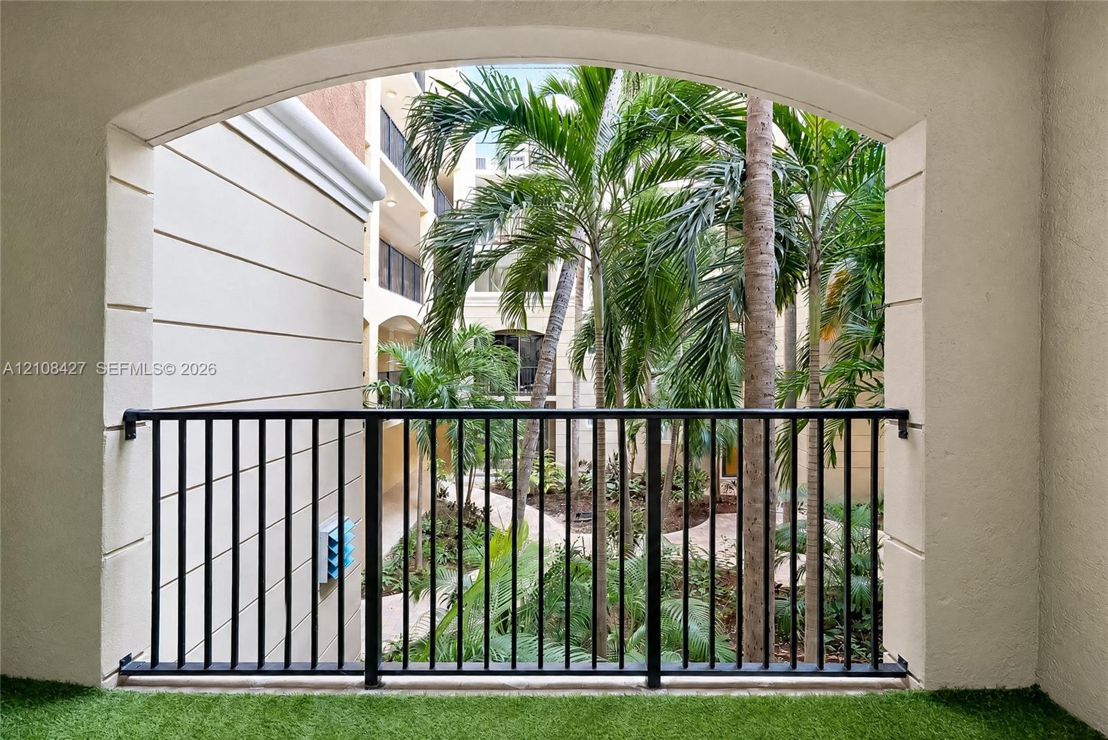 Covered balcony featuring a decorative arched entryway, stucco walls, and a black metal railing