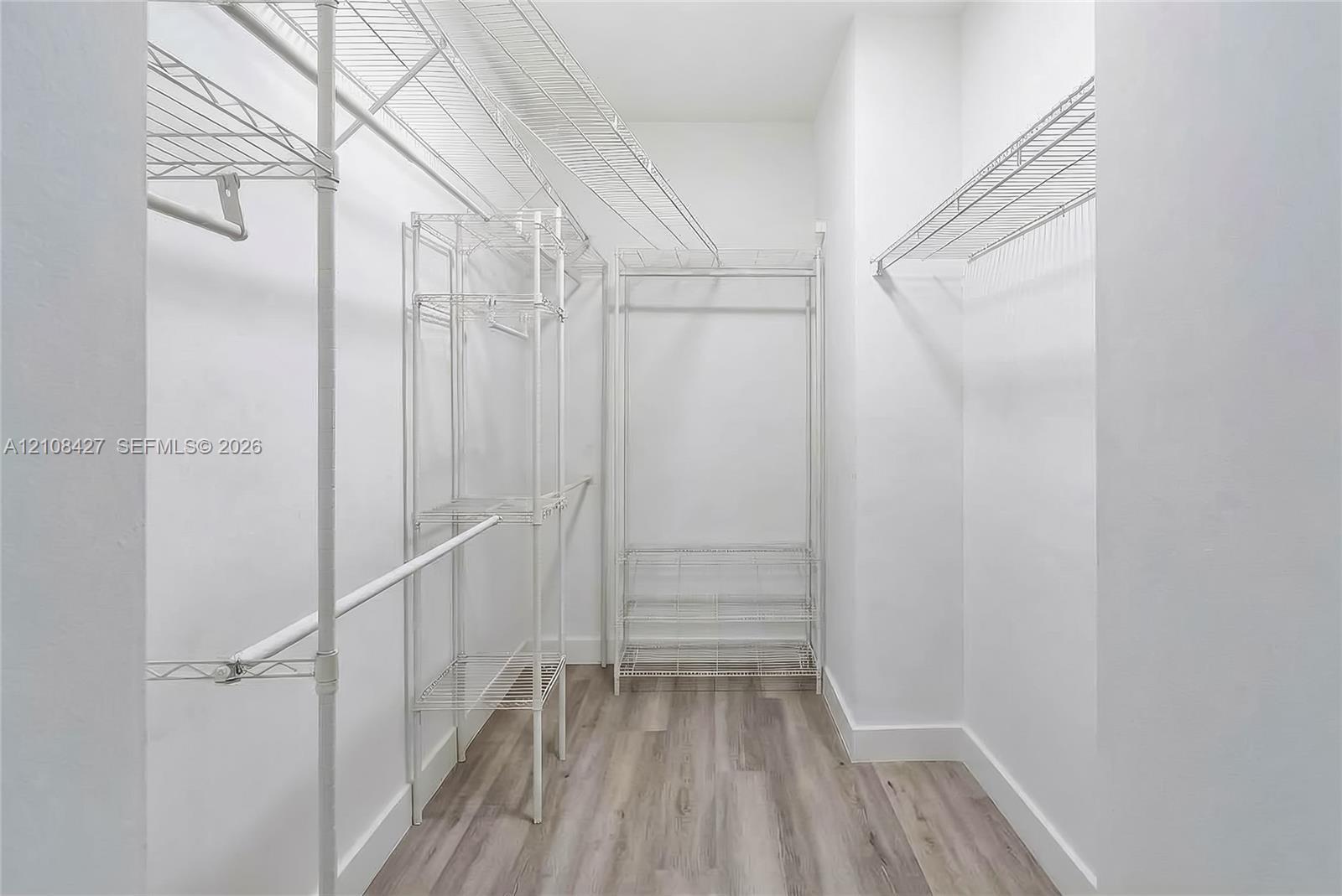 Walk-in closet featuring multi-tiered white wire shelving, hanging rods, integrated shoe storage, and wood-finish flooring