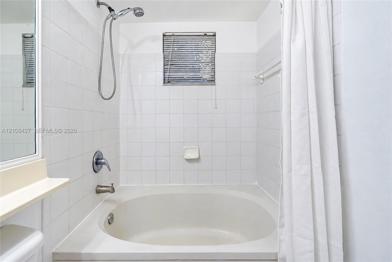 Built-in soaking tub with ceramic tile surround, integrated shower fixture, and wall-mounted soap dish