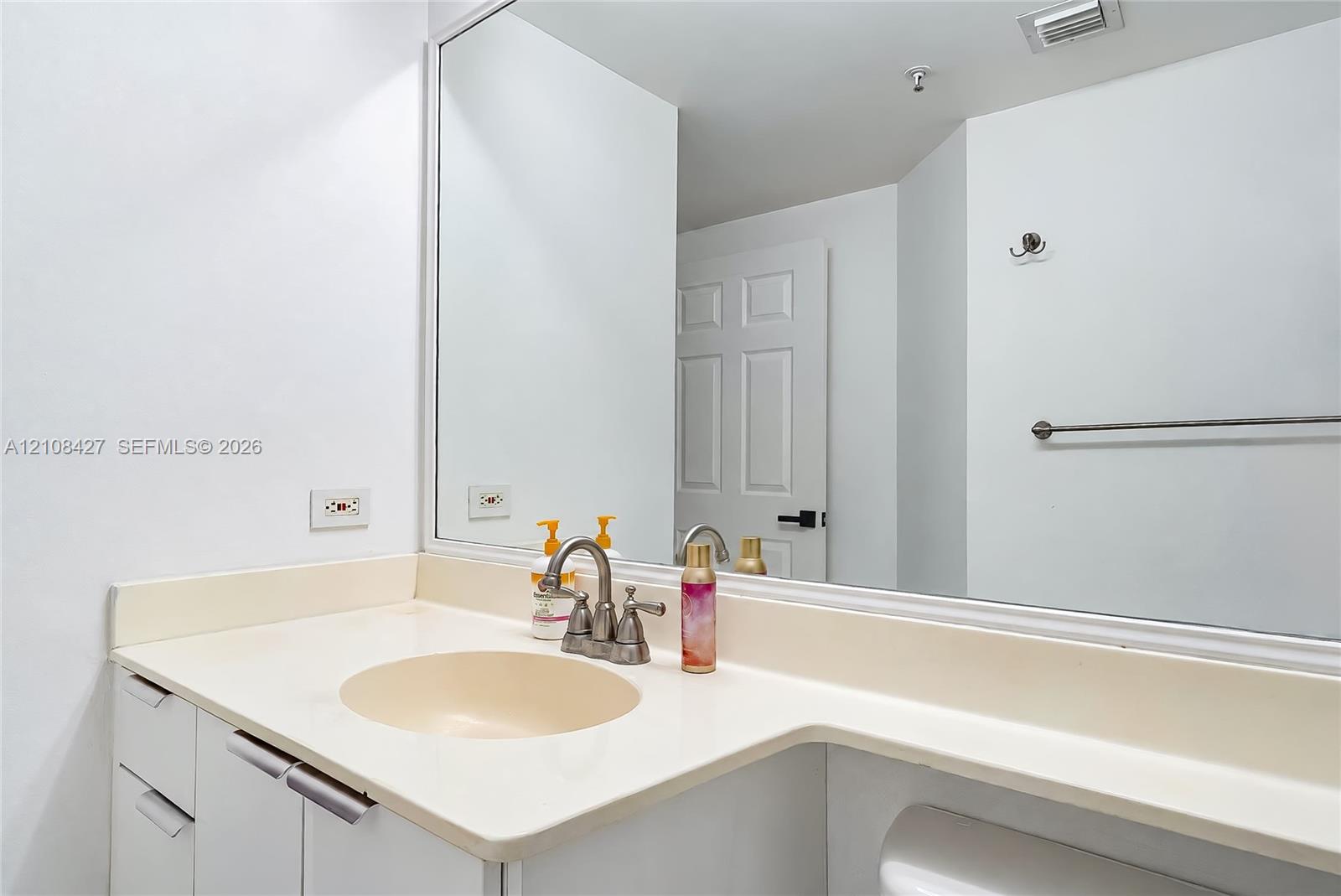 Bathroom vanity featuring an integrated countertop and basin, dual-handle metal faucet, expansive wall-mounted mirror, and cabinet storage