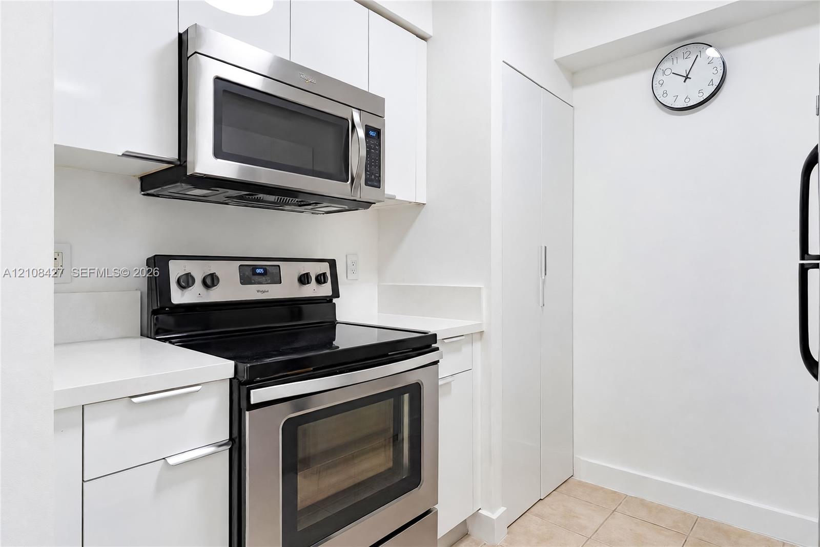 Kitchen featuring white cabinetry, stainless steel microwave, black electric range, and solid-surface countertops