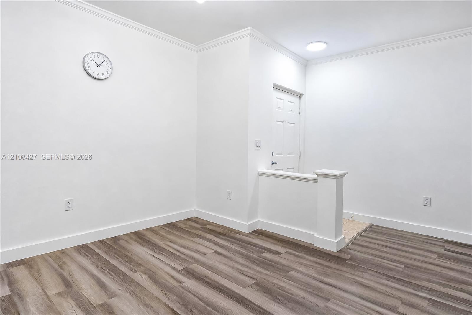 Wood-finish flooring, crisp white walls, crown molding, and a solid-panel door with architectural half-wall trim