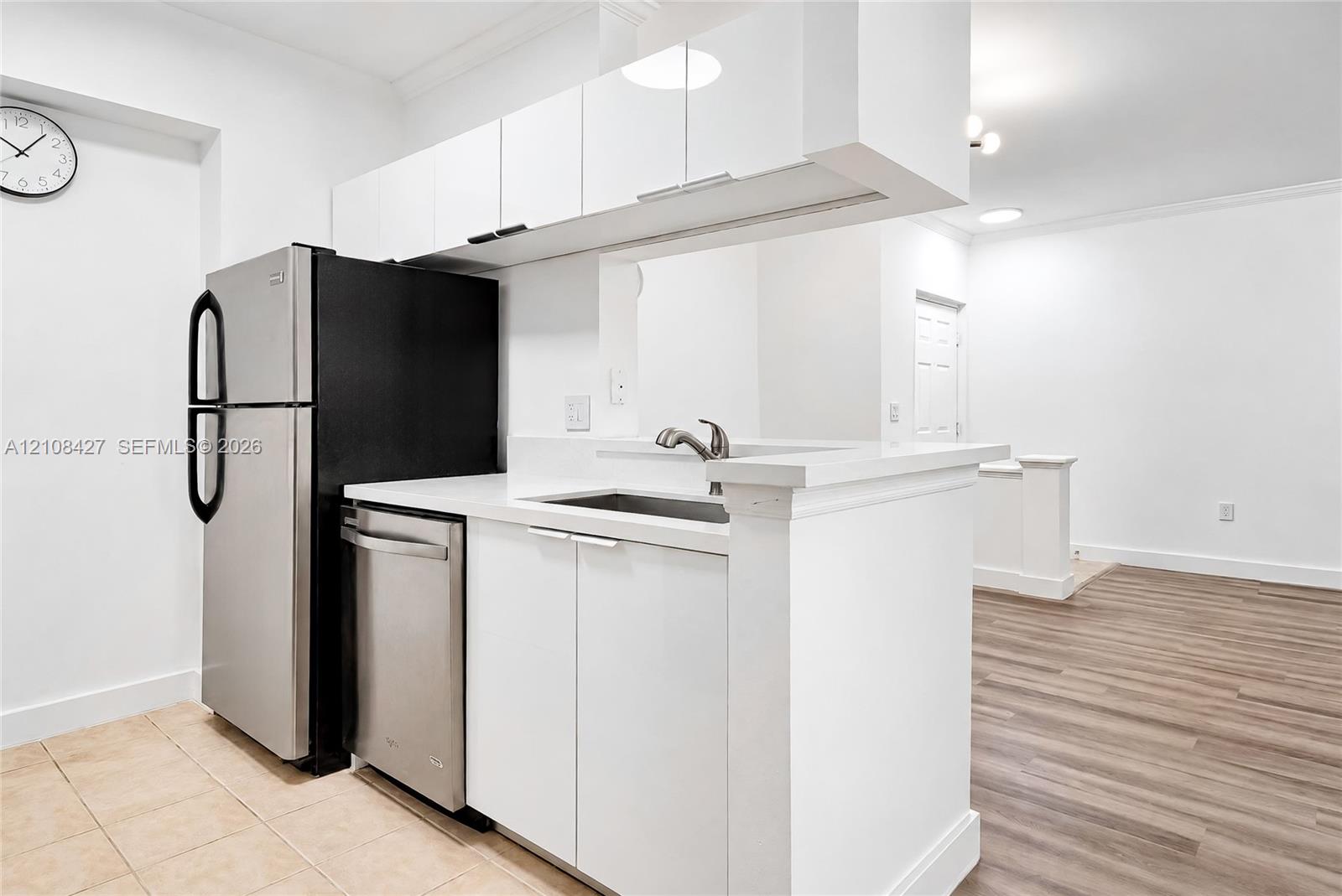 Kitchen featuring white flat-panel cabinetry, stainless steel appliances, wood-finish flooring, and a pass-through counter