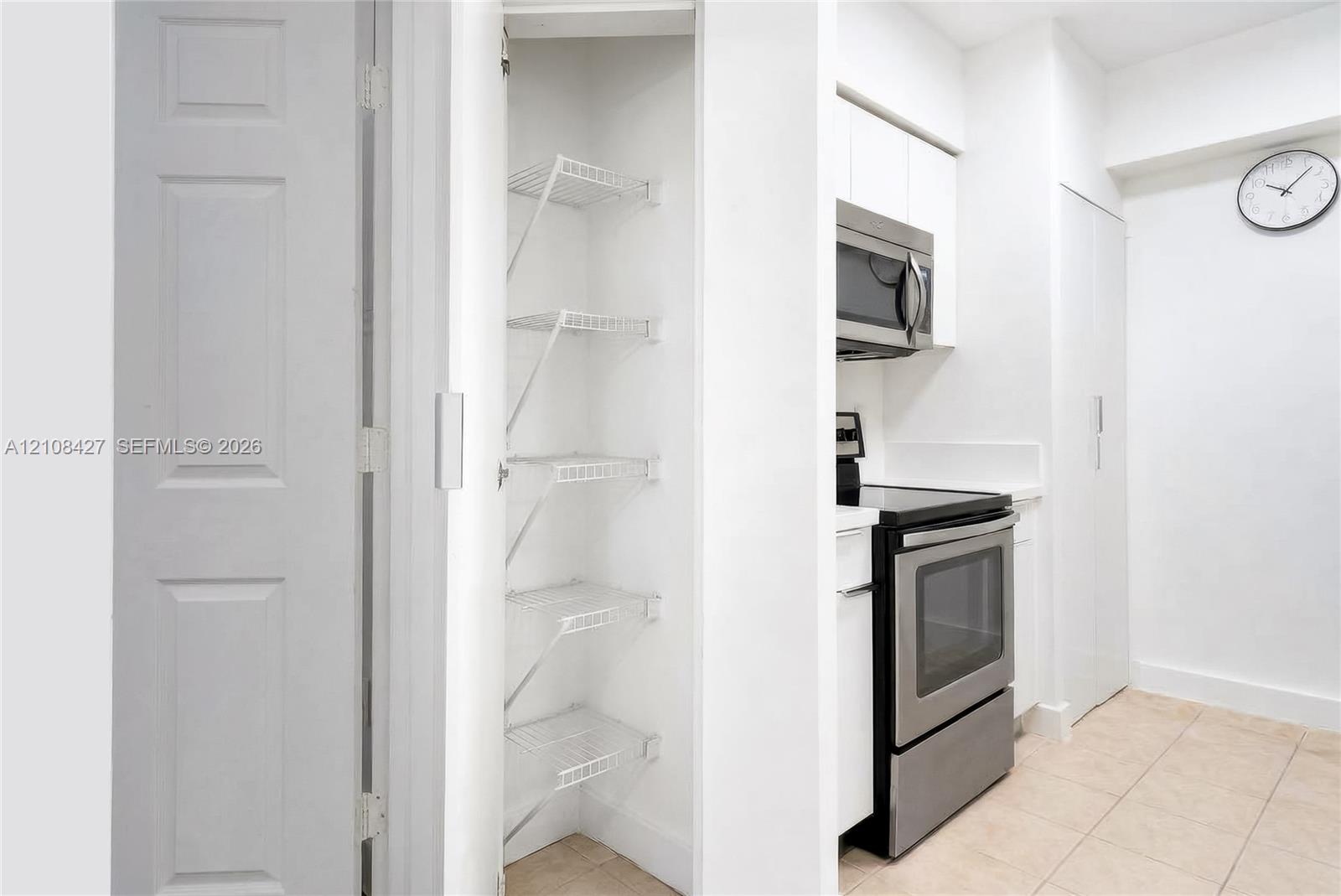Pantry featuring white wire shelving, stainless steel microwave and range, white cabinetry, and tile flooring