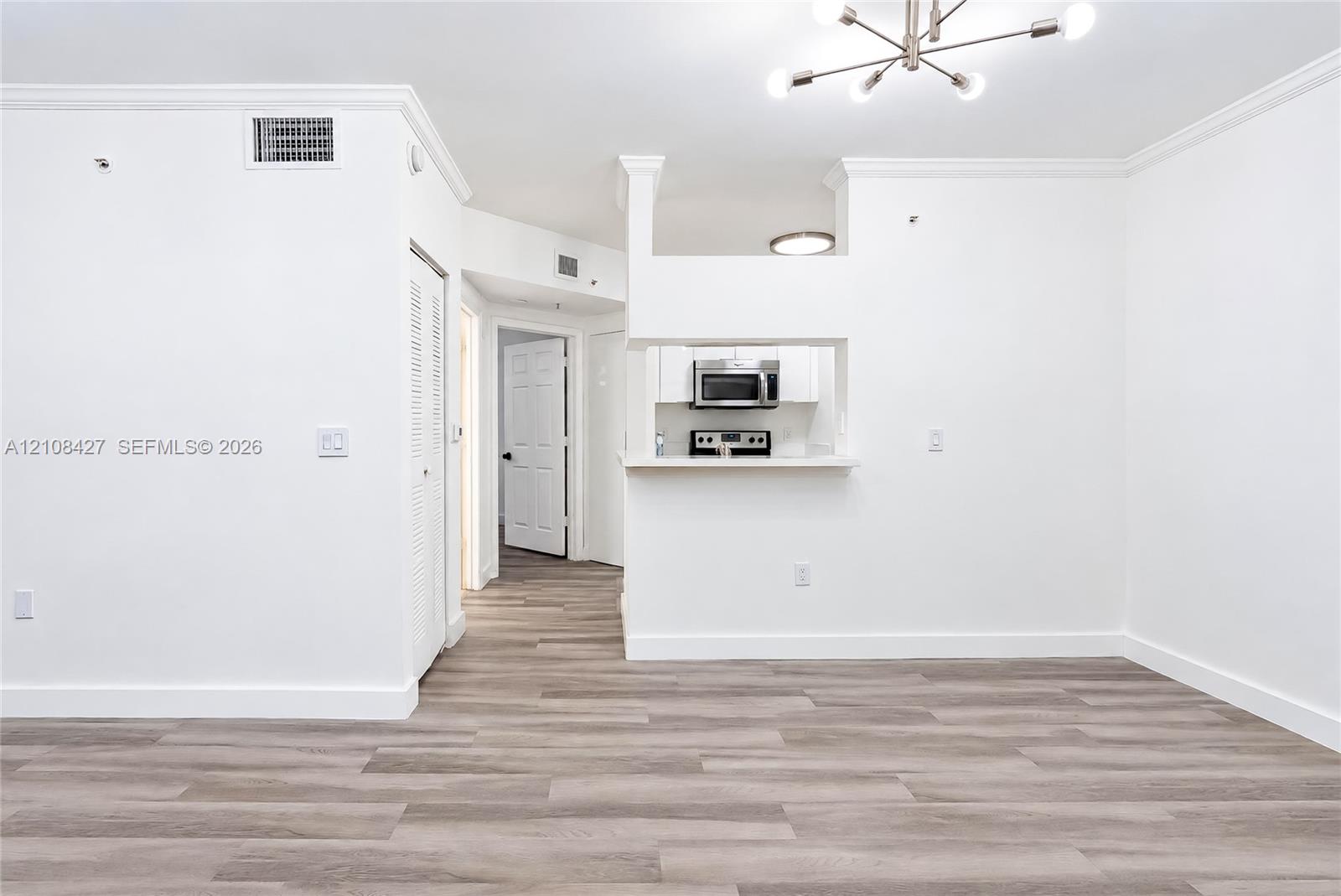 Interior space featuring wood-finish flooring, crown molding, a modern multi-arm chandelier, and a kitchen pass-through window with built-in appliances