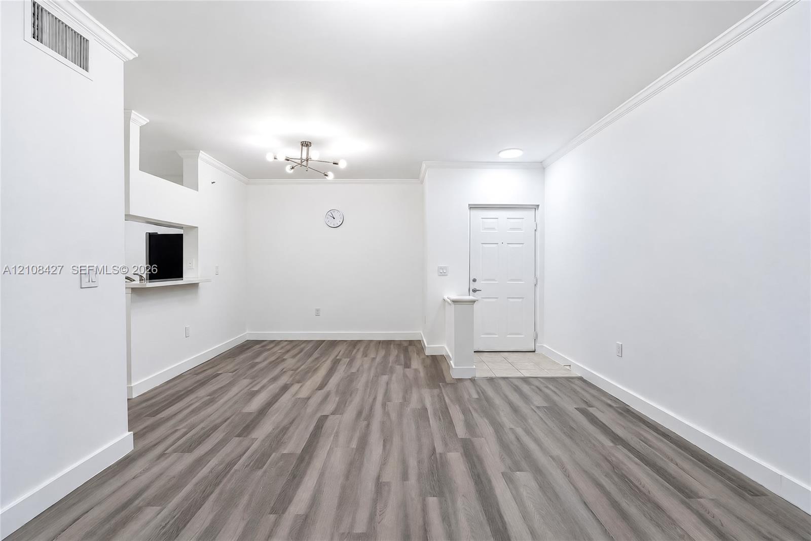 Open-concept interior featuring wood-finish flooring, crown molding, a multi-arm modern light fixture, and a pass-through opening