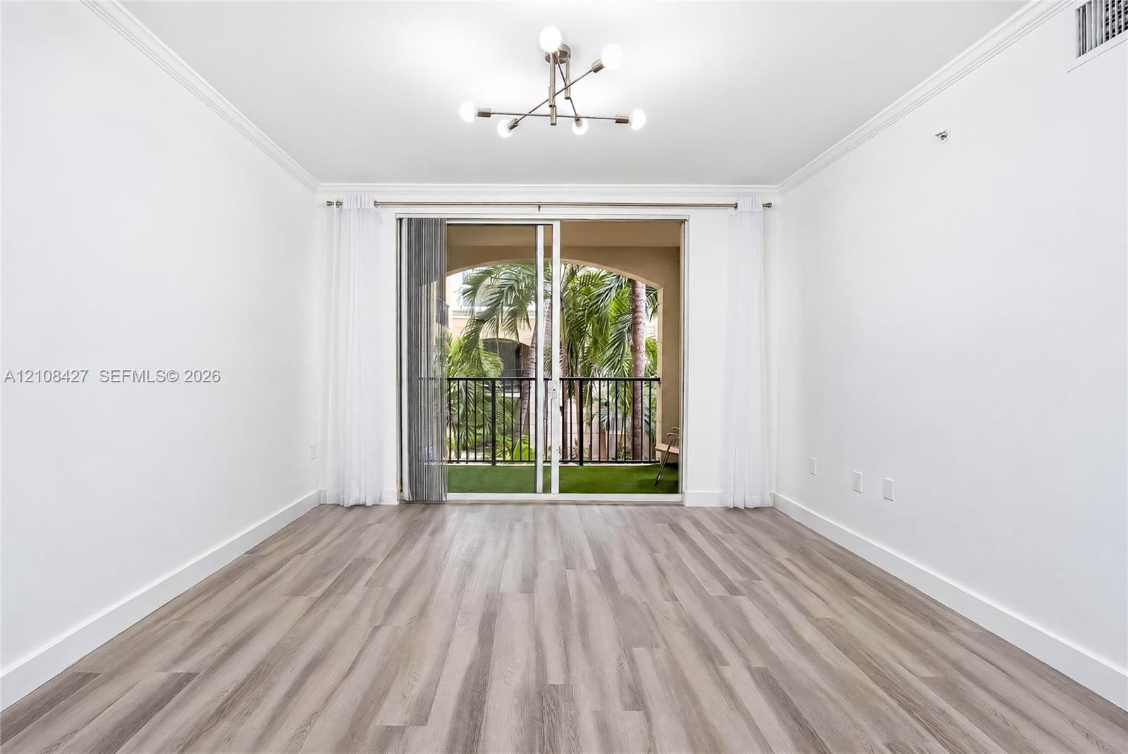 Interior featuring wood-finish flooring, crown molding, multi-arm chandelier lighting, and a sliding glass door opening to a private balcony with an arched architectural detail