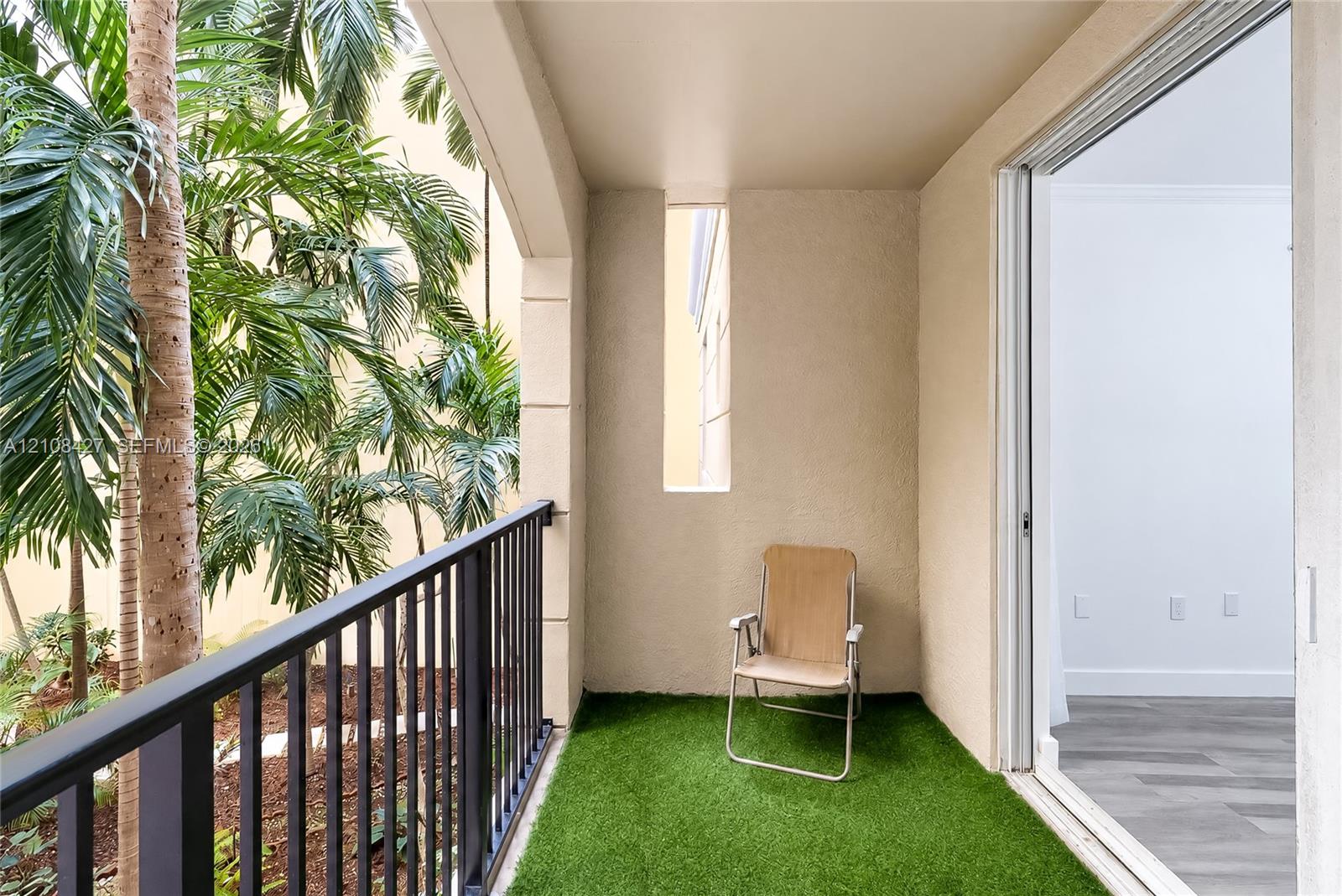 Covered balcony featuring a black metal railing, synthetic turf flooring, textured stucco wall finish, and a vertical architectural cutout