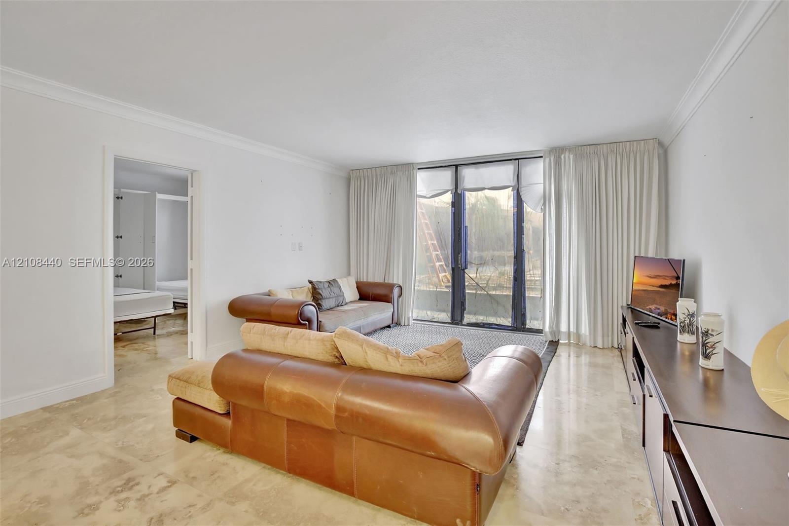 Living space featuring polished stone flooring, crown molding, and floor-to-ceiling glass sliding doors