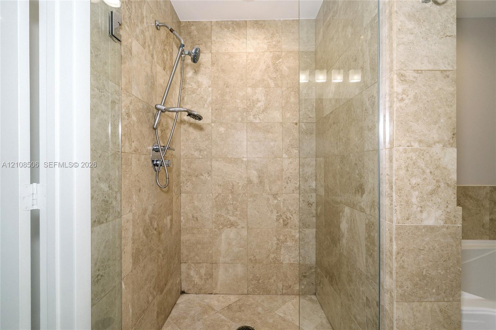 Walk-in shower featuring floor-to-ceiling stone tile, a glass enclosure, and a multi-setting handheld shower fixture
