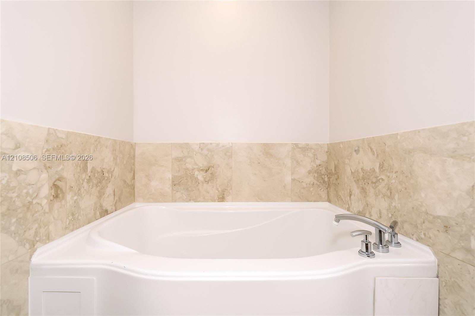Built-in soaking tub with a polished chrome deck-mounted faucet, surrounded by neutral-toned stone tile wainscoting