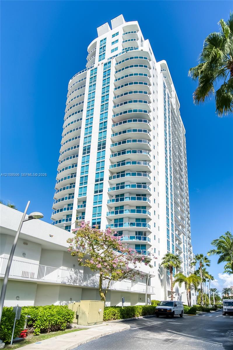 High-rise building featuring a white concrete facade, tinted glass windows, and wrap-around balconies on each level