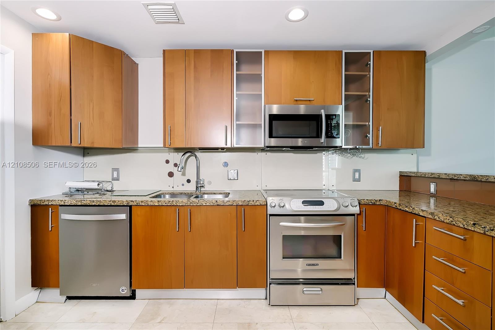 Kitchen featuring wood-finish cabinetry, stone-surface countertops, stainless steel appliances, glass-front upper cabinet doors, and recessed ceiling lighting
