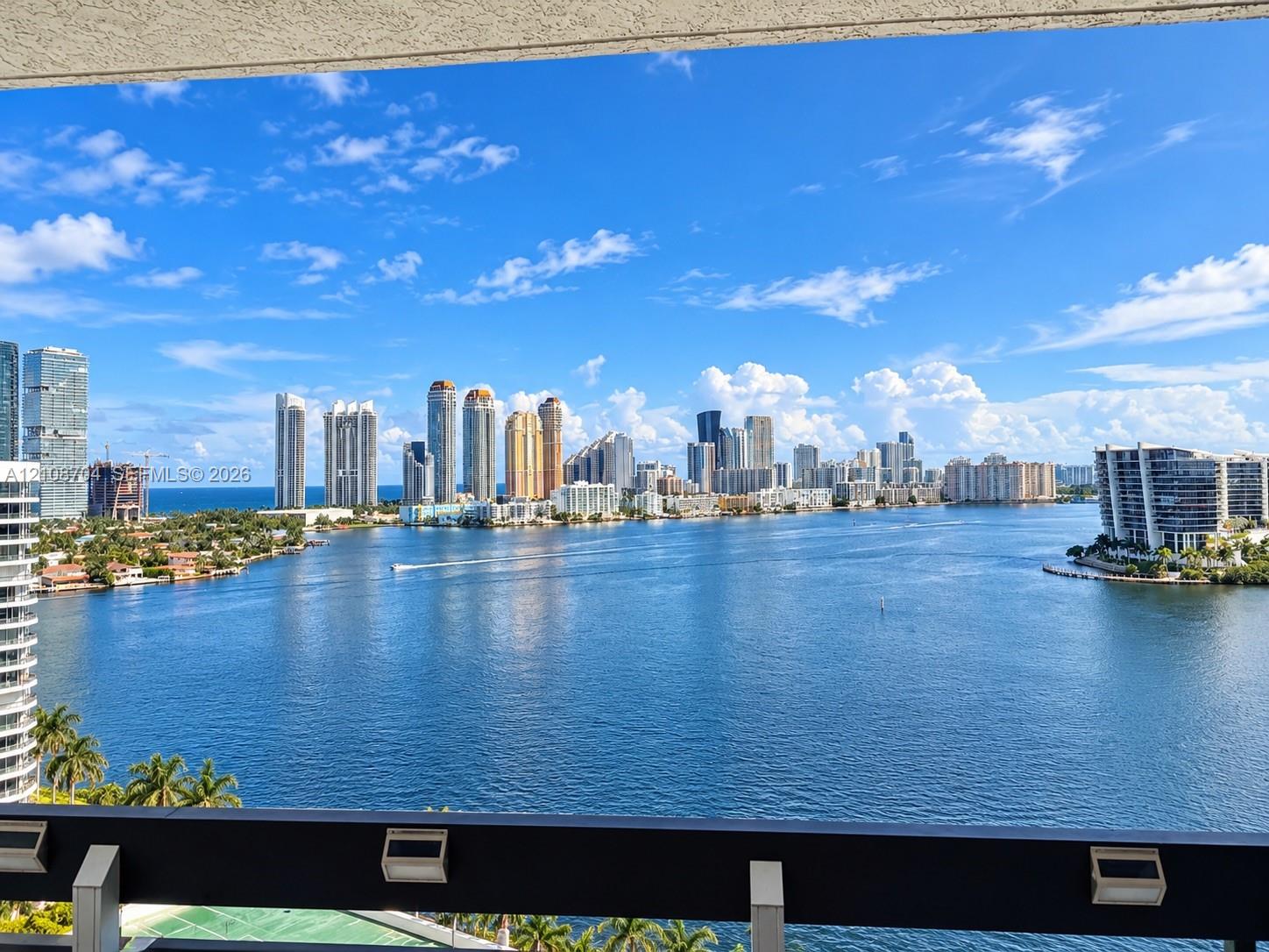 Outdoor balcony featuring a dark metal railing with integrated lighting, overlooking a wide expanse of water and a skyline