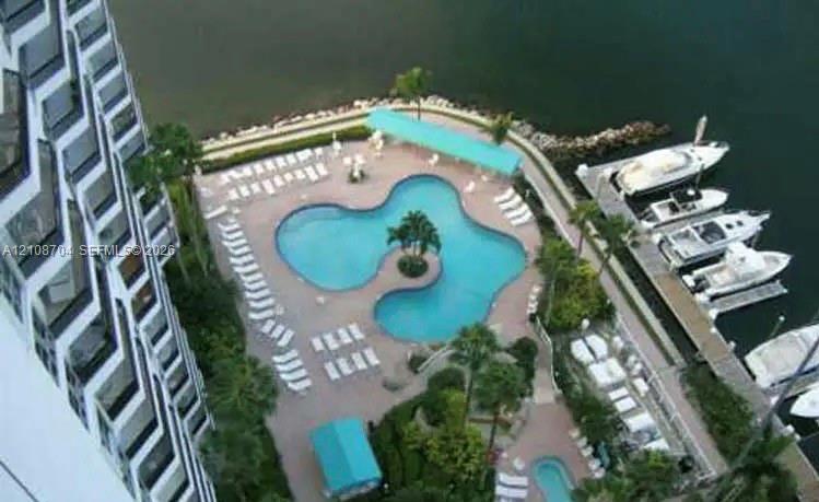 Waterfront pool deck featuring a curvilinear swimming pool, private boat slips, concrete decking, and tropical landscaping