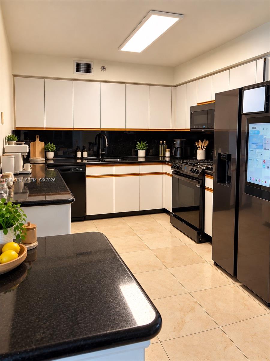 Kitchen featuring white flat-panel cabinetry, dark stone countertops, tile flooring, and integrated black appliances