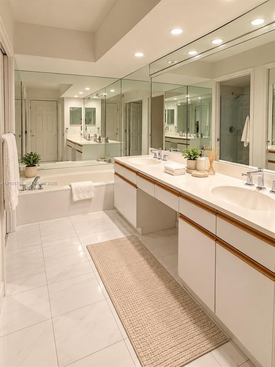 Bathroom featuring dual-sink vanity with light-tone countertops, full-wall mirrors, a built-in soaking tub, and large-format tile flooring
