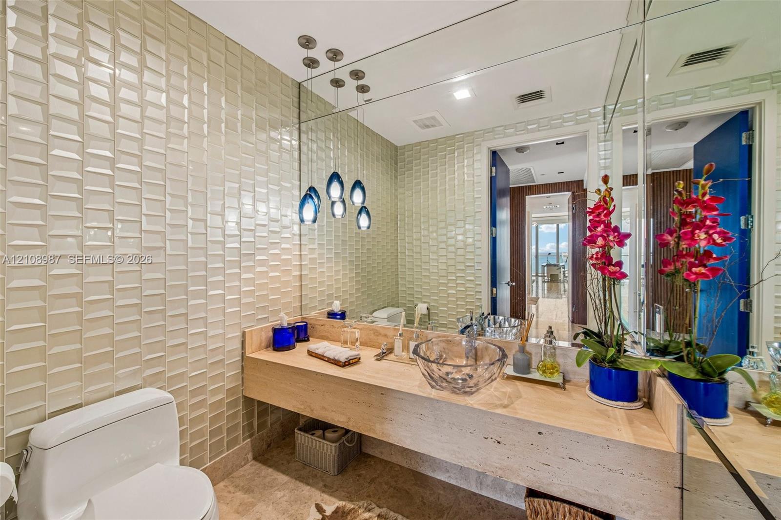 Full-height dimensional tile wall, floating natural-stone countertop, glass vessel sink, and teardrop pendant lighting